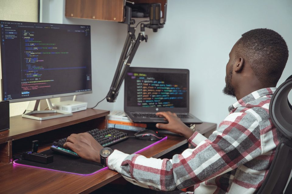 A developer writing code across a laptop and a desktop screen in a Nairobi office