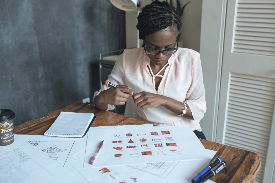 A designer at a wooden desk covered in printed icon and logo sketches